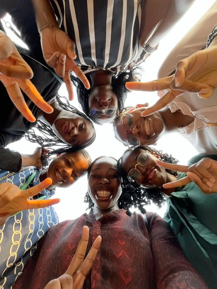 Six smiling young women photographed from below, making peace signs in a circle