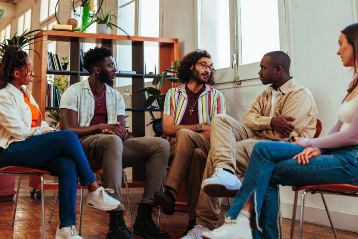 A group of people talking together in a circle of chairs in a bright community room